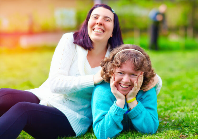 Two girls sitting on the grass smiling at the camera